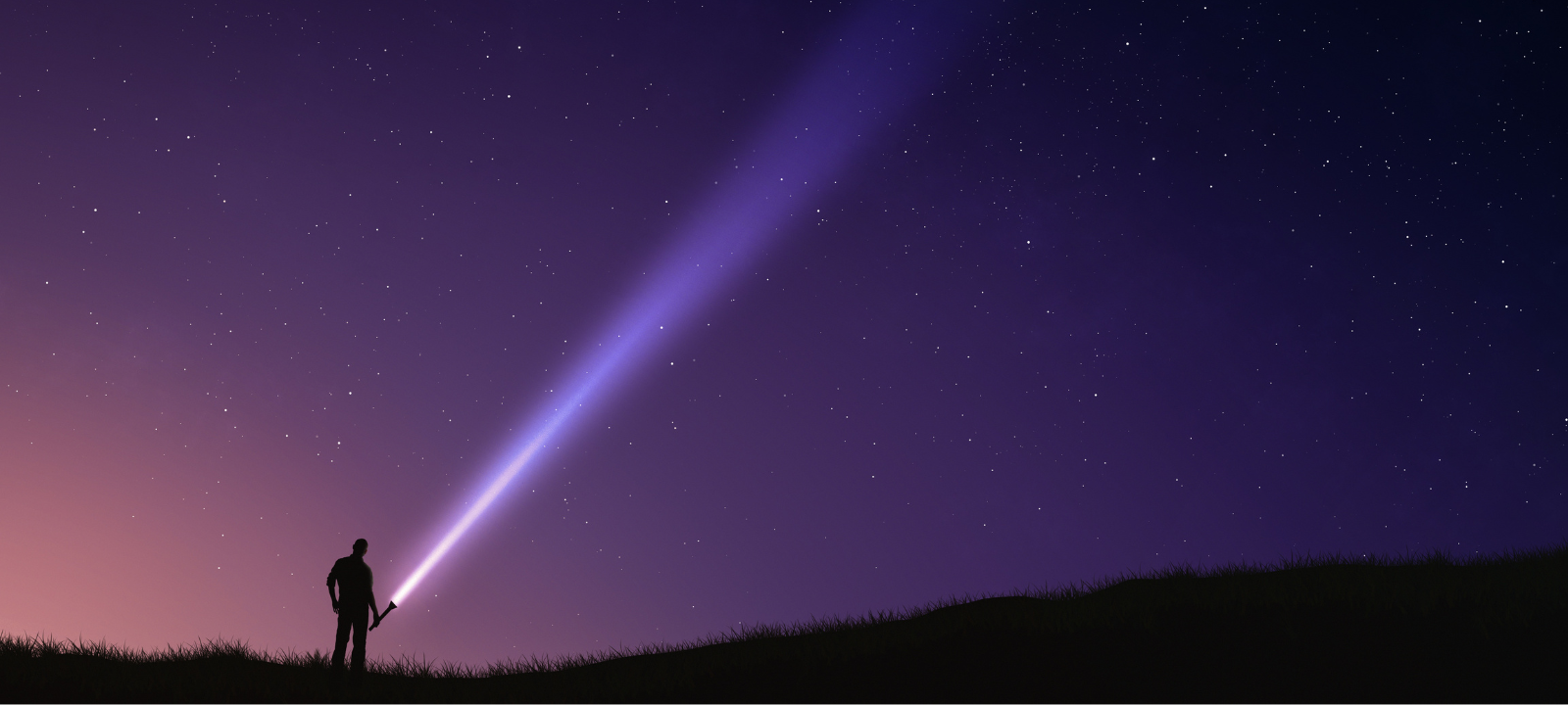 A silhouette of a person standing on a dark ridge, using the flashlight to shine a bright beam of light into a vibrant purple and starry night sky. 