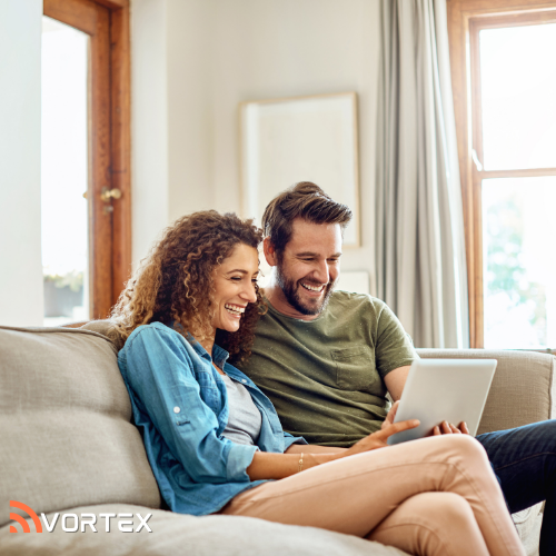 A smiling man and woman sit together on a couch, looking at a digital tablet with the "Vortex" logo in the bottom corner.